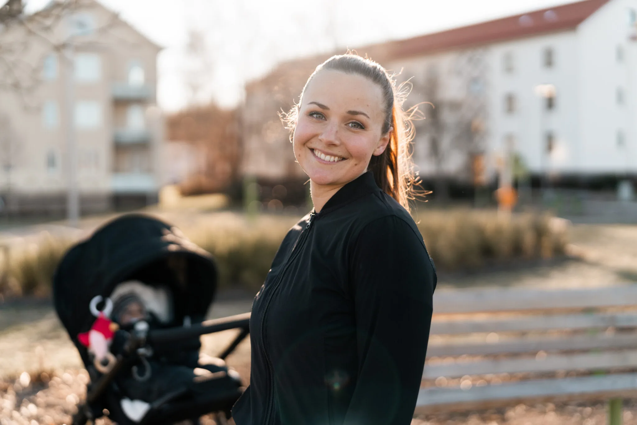 Ung mor smiler utenfor sitt nye hjem med en barnevogn i bakgrunnen